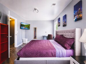 A modern bedroom with a large bed, a TV, and artwork on the walls. - 2BR · High Point · Hickswood Townhome (High Point)