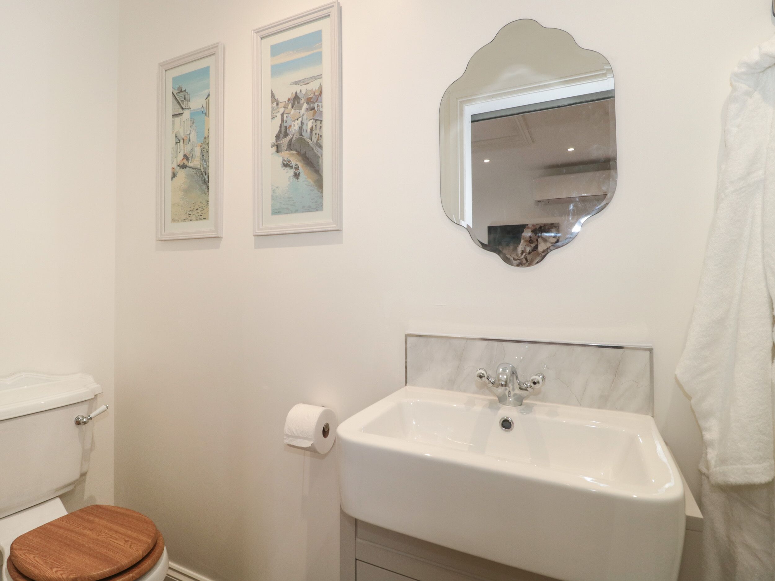 A bathroom with a white sink, wooden toilet seat, and two framed paintings on the wall.