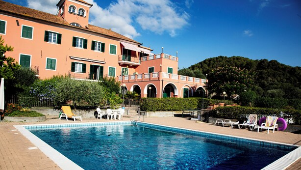 Une piscine avec des chaises longues et, au fond, un bâtiment doté d’un balcon.