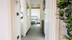 Un couloir avec un radiateur, un lit recouvert d’une couverture verte et une porte dotée d’un miroir.