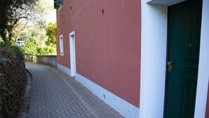 Un chemin pavé mène à une porte verte bordée de blanc, qui se trouve à côté d’un bâtiment rouge avec une base blanche et une petite fenêtre.