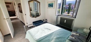 Une chambre à coucher avec un lit, une fenêtre donnant sur un paysage agréable, un radiateur et une porte menant à une autre pièce.
