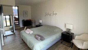 A spacious bedroom with a large bed, a chair, a nightstand, and a wall-mounted lamp.