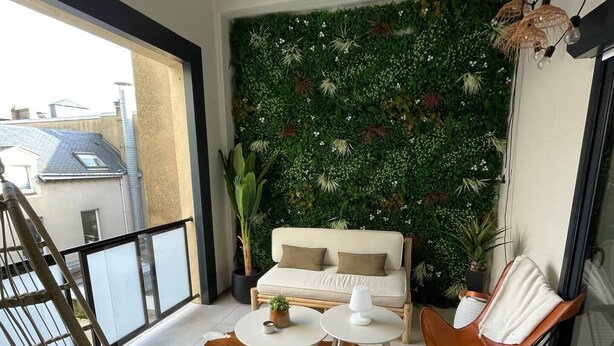 A balcony with a white sofa, two white round tables, a brown leather chair, a hanging light fixture, and a green vertical garden wall.