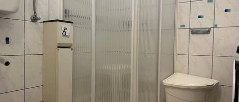 A bathroom with a shower enclosure, a toilet, and a yellow stool.