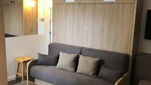 Una habitación moderna con un sofá gris, un mueble de madera y un taburete pequeño de madera.