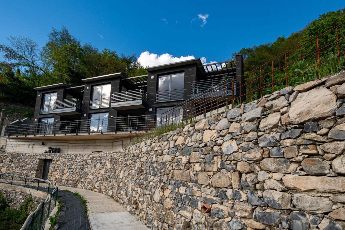 Een modern huis met twee verdiepingen, een stenen keerwand, een metalen trap en een pad dat naar de ingang leidt.