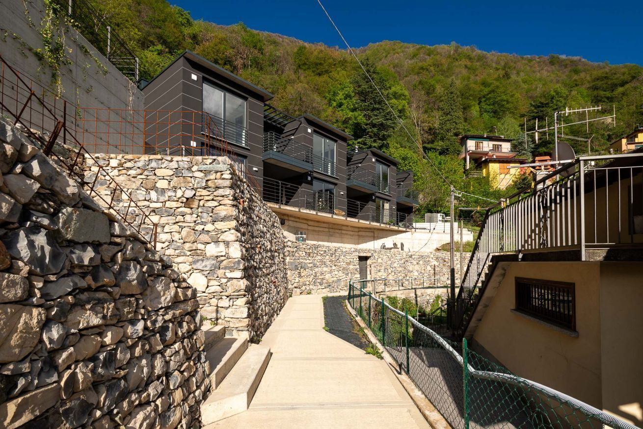 Un edificio moderno con varios balcones, un muro de piedra de contención y un camino que lleva a una entrada porticada.