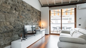Een moderne woonkamer met een stenen muur, een flatscreen televisie, een witte console tafel en een grijze bank.