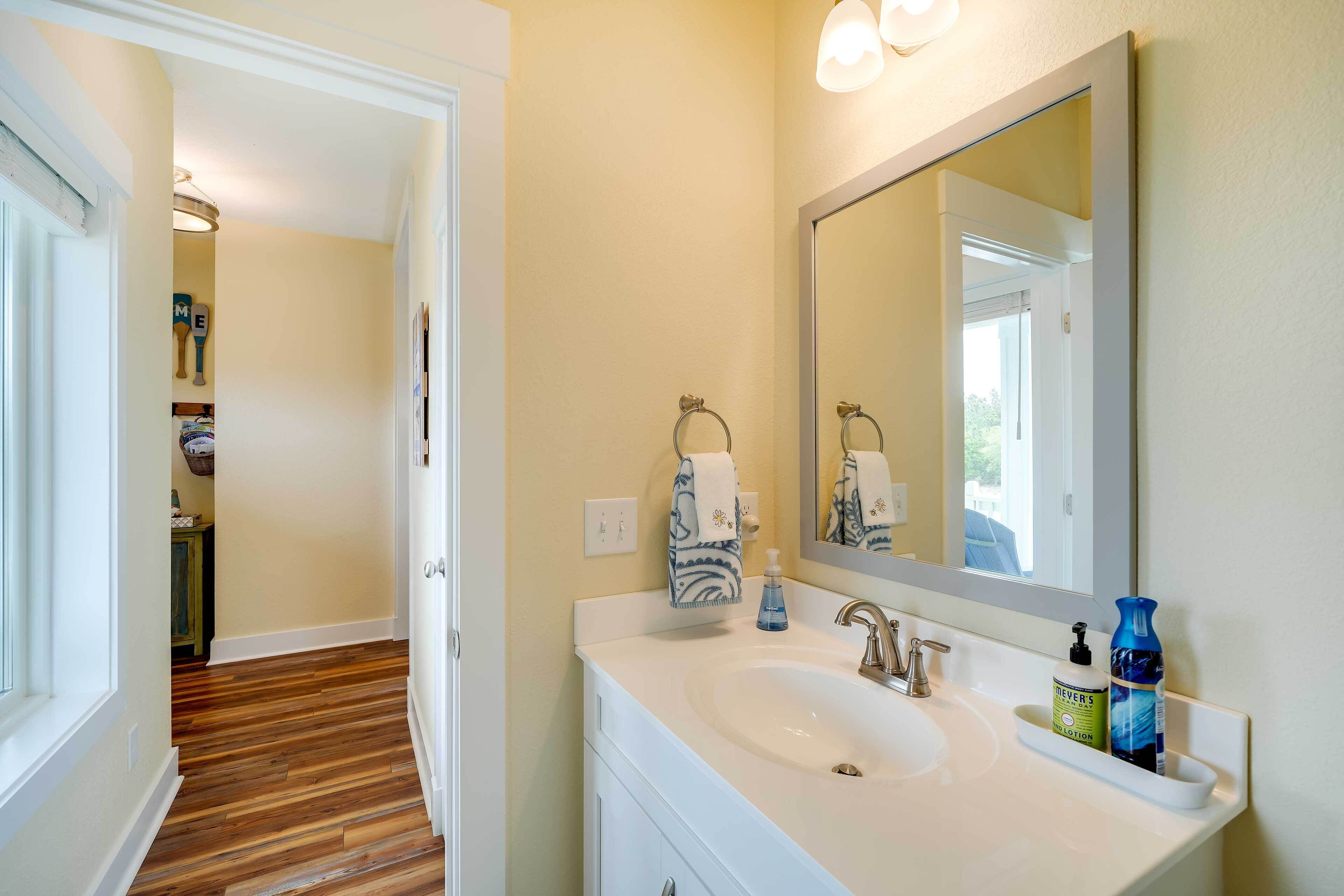 A bathroom with a white sink, a mirror, and a wooden floor leading to a hallway.