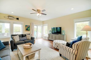 A spacious living room with a ceiling fan, a television, and a large window.