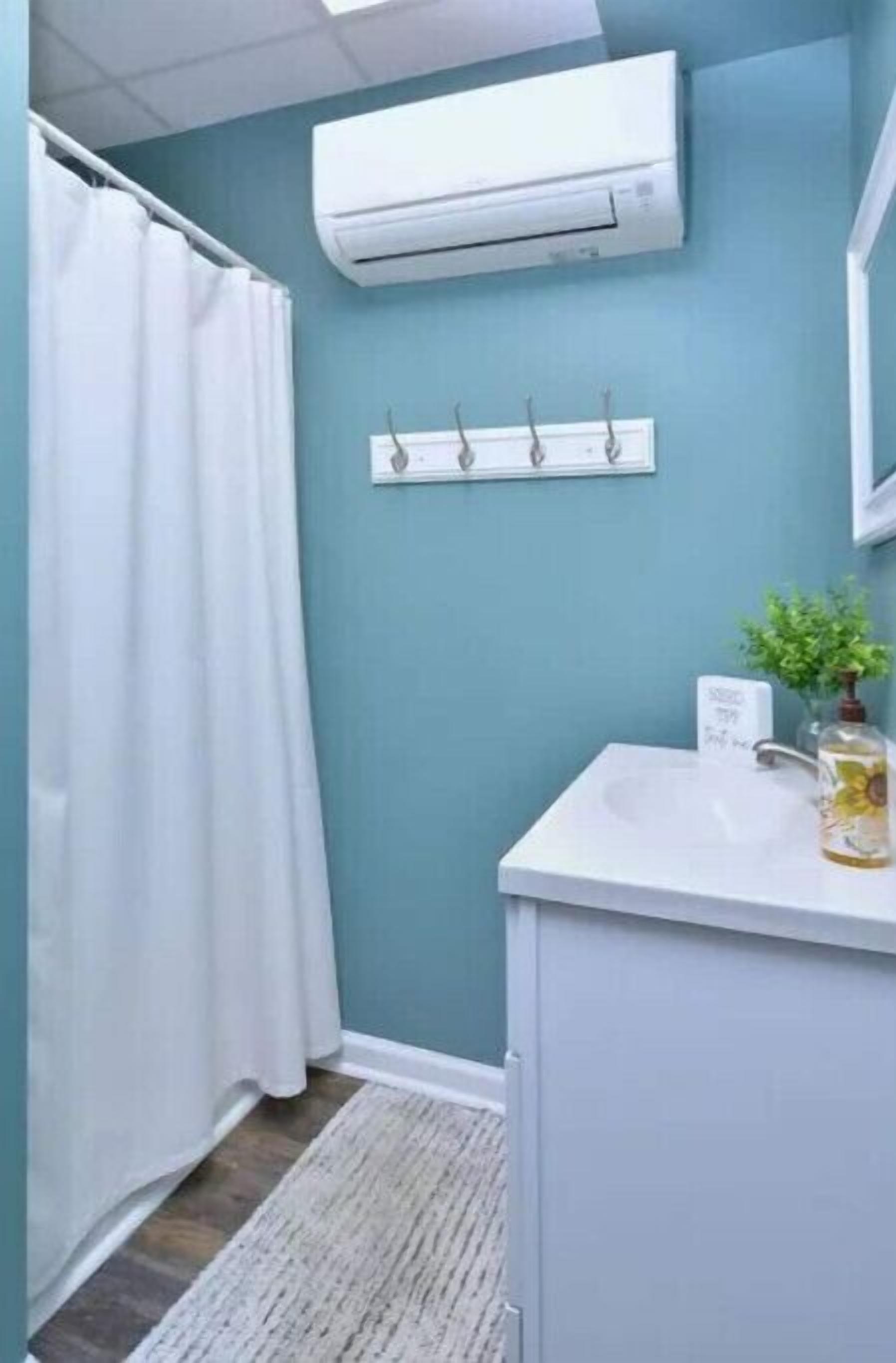 Un baño con un lavabo blanco, un espejo, un perchero para toallas y un equipo de aire acondicionado.