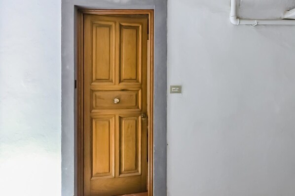 Eine geschlossene Holztür mit einem schlichten Griff, einem Lichtschalter an der rechten Wand und einer kleinen Fuge unten.