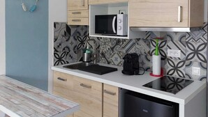 A modern kitchen with light wood cabinets, a black dishwasher, a microwave, and a sink with a black countertop. - Gloria Maris Apartment (Menton)