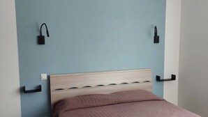 A bedroom with a wooden headboard, a brown quilted bedspread, and two wall-mounted nightstands with black lamps. - Gloria Maris Apartment (Menton)