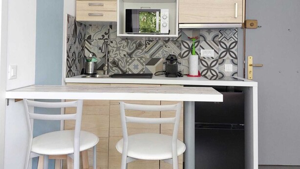 A modern kitchen with two white chairs, a microwave, and a black dishwasher. - Gloria Maris Apartment (Menton)