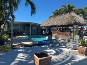 Un espace piscine agrémenté d’une structure à toit de chaume, de chaises longues et de plantes en pot.