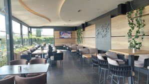 A modern restaurant with a long counter, cushioned seating, and a large TV screen. - Hotel Grand (Banja Luka)
