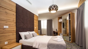 A modern hotel room with a large bed, wooden paneling, a desk, and a mirror. - Hotel Grand (Banja Luka)