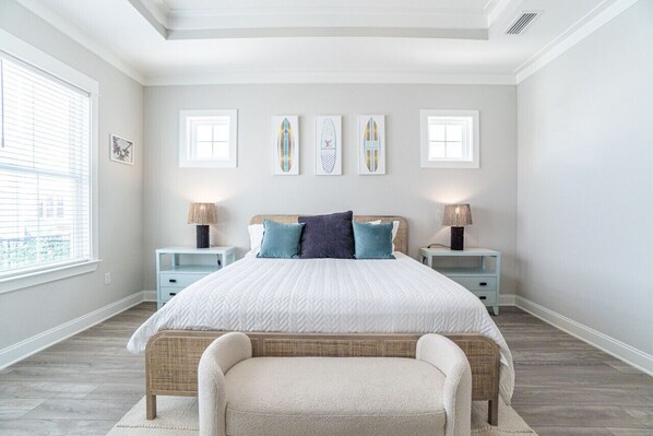A bedroom with a large bed, two nightstands, a wicker chair, and framed artwork on the wall.