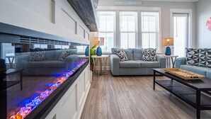 A modern living room with a fireplace, grey sofas, and a decorative fish tank. - Luxury 4BR/4BA Beach Retreat Game Room, Resort Pool, & Prime Location (Orange Beach)