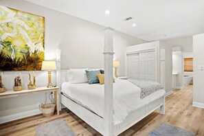 A spacious bedroom with a four-poster bed, a wooden nightstand, and a large abstract painting.