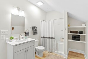 A modern bathroom with a white sink, toilet, and shower area. There are shelves with towels and toiletries.