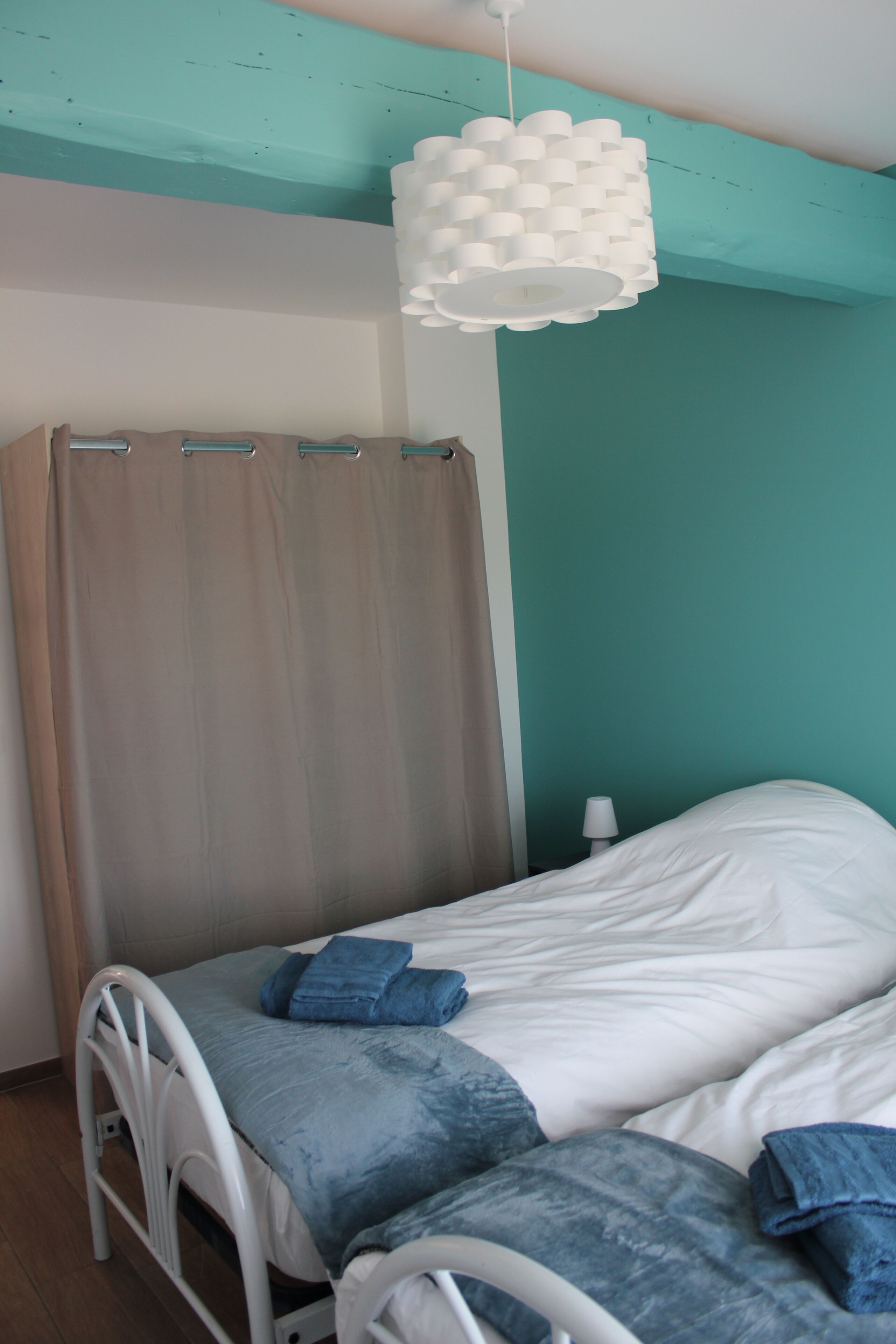 Una cama individual con cabecera blanca, una colcha azul y una lámpara colgante blanca.