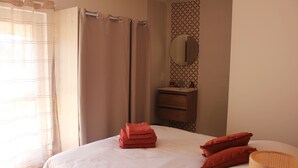 Une chambre à coucher avec un lit, une table de chevet, un miroir et une fenêtre avec des rideaux.