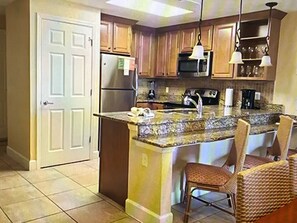 Kitchen with central island, sink, and microwave, featuring two chairs and a door.