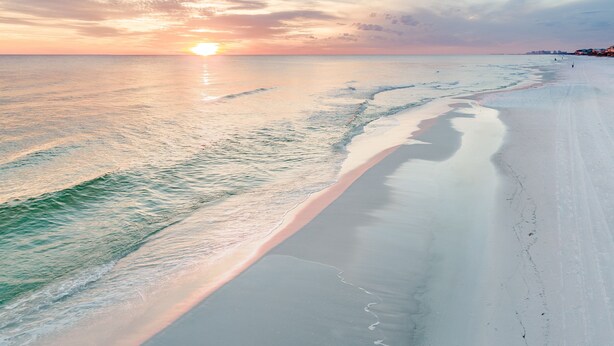 Ein Strand mit freiem Blick auf den Ozean und einem Sonnenuntergang im Hintergrund.