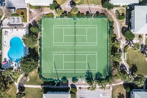 An aerial view of a property with a tennis court, a swimming pool, and surrounding greenery.