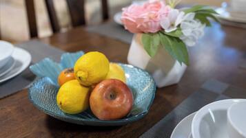 Une table sur laquelle se trouve un saladier en verre bleu rempli de fruits, un vase avec des fleurs et une nappe à carreaux.