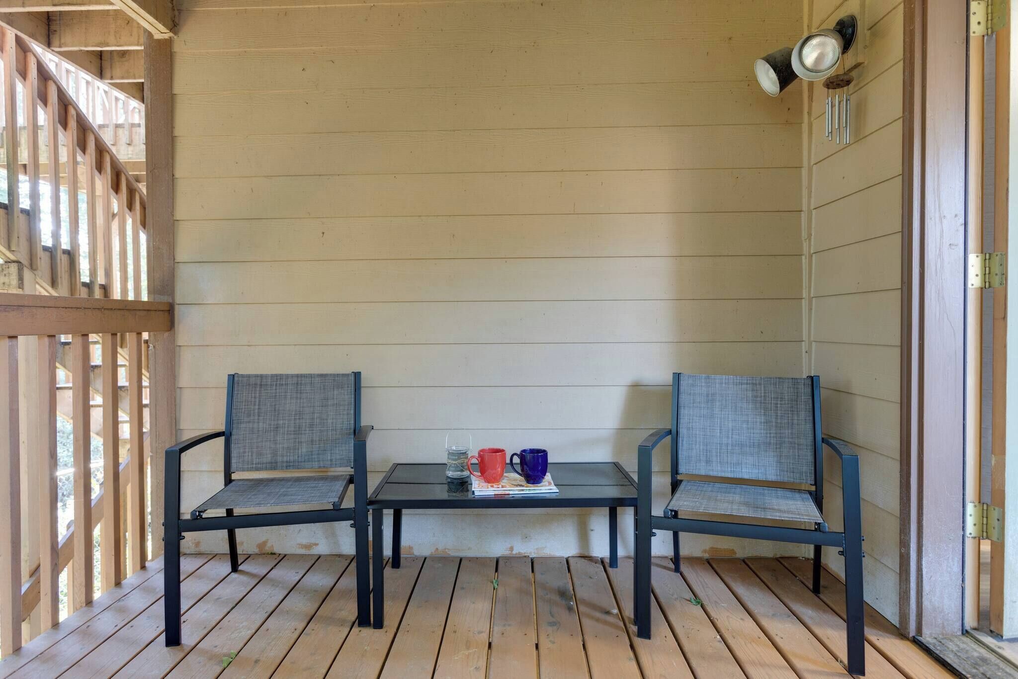 Une terrasse en bois avec deux chaises et une table, une petite lampe de table et une vue sur une balustrade en bois.