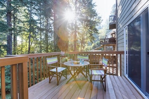 A wooden deck with a table and chairs, surrounded by trees, and a building with a balcony. - Oregon Jade Lodging- Spacious 2 Bedrooms, Ev Charger, Quite By Stream (West Linn)
