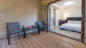 A room with a bed, a nightstand, a lamp, and a sliding glass door leading to a balcony with two chairs and a small table. - Oregon Jade Lodging- Spacious 2 Bedrooms, Ev Charger, Quite By Stream (West Linn)