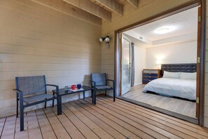 Ein Zimmer mit einem Bett, einem Nachttisch, einer Lampe und einer Glastür, die auf einen Balkon mit zwei Stühlen und einem kleinen Tisch führt.