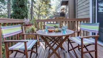 A wooden deck with a round table and striped chairs, surrounded by potted plants and a view of a building.