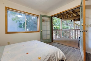 A bedroom with a bed, a window, a door leading to a balcony, and a view of trees. - Oregon Jade Lodging- Spacious 2 Bedrooms, Ev Charger, Quite By Stream (West Linn)