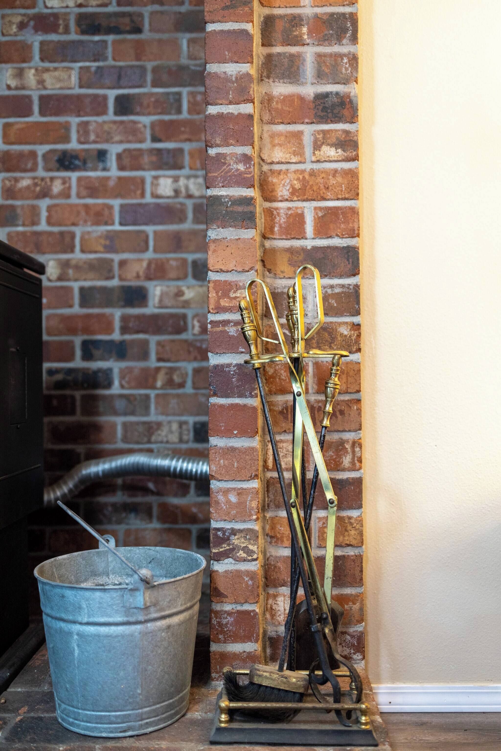 A brick wall, a metal bucket, and a brass tool stand.