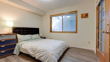 A bedroom with a bed, dresser, nightstand, lamp, window, and door.