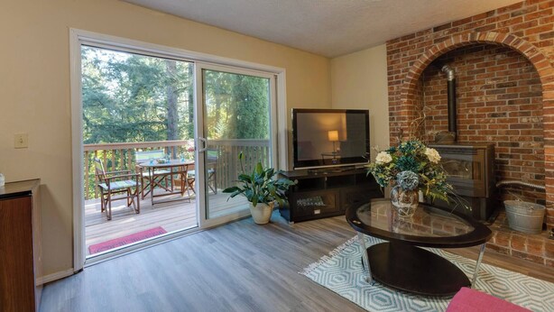 A living room with a TV, fireplace, and a sliding glass door leading to a balcony. - Oregon Jade Lodging- Spacious 2 Bedrooms, Ev Charger, Quite By Stream (West Linn)