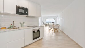 Una cocina moderna con armarios blancos, un microondas integrado y un horno. Se observa un área de comedor con una mesa y sillas al fondo.