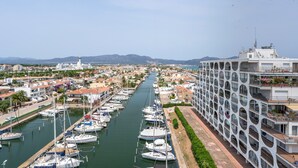 Un puerto deportivo con varias embarcaciones amarradas a lo largo de un canal, rodeado de edificios residenciales y un gran edificio blanco con un diseño circular único en la ventana.