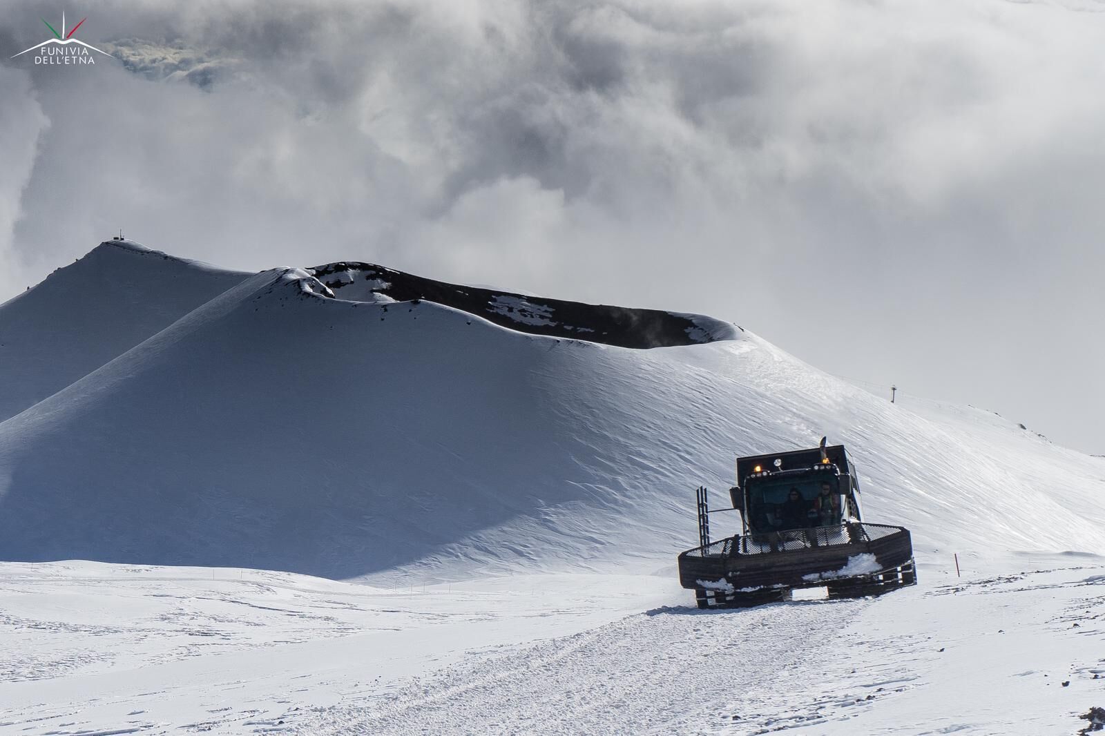 Ein schneebedeckter Berg mit einer Seilbahn und einem Fahrzeug, das Skifahrer befördert.