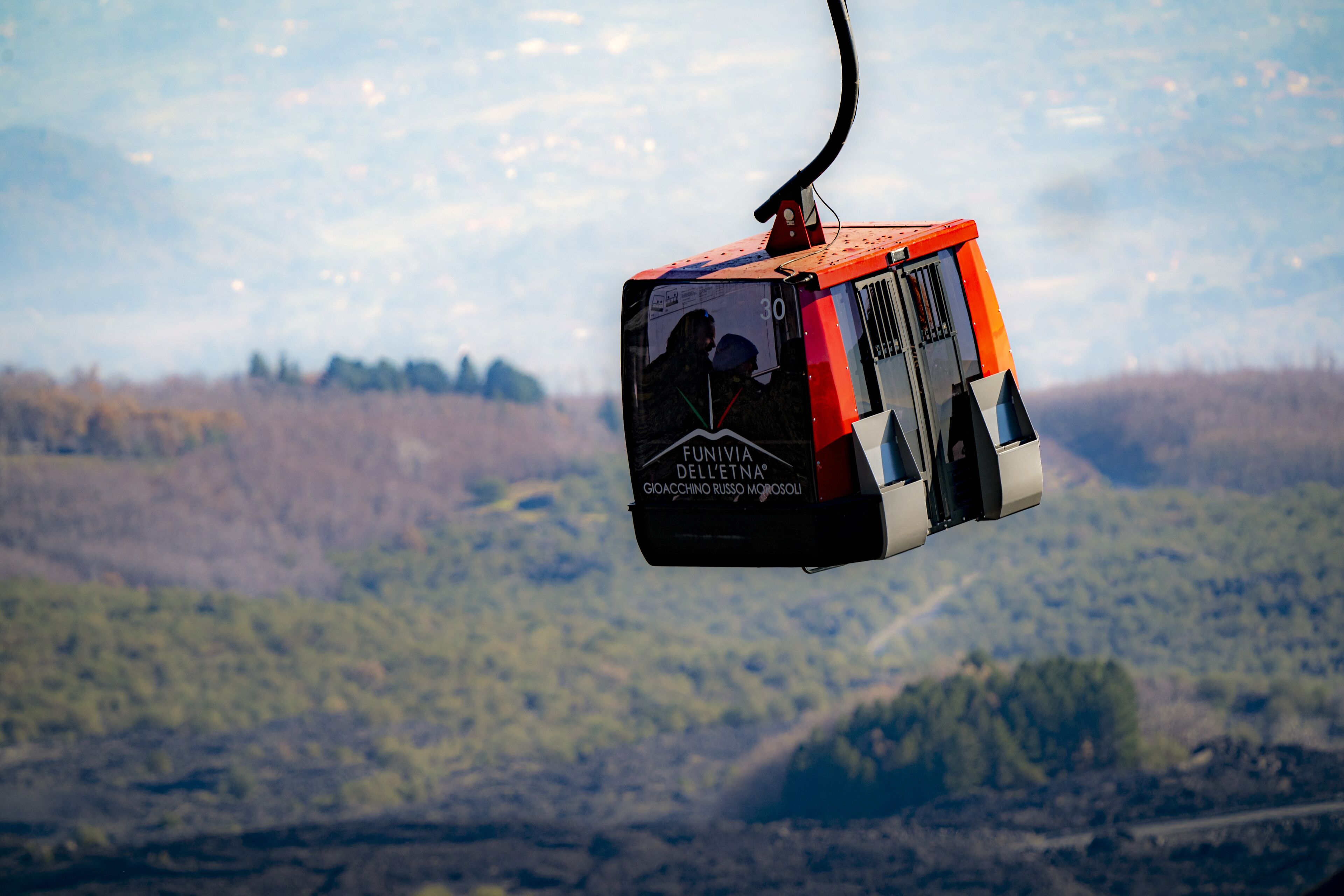 Une télécabine arborant les inscriptions « FUNIVIA DELL’ETNA » et « GIOACCHINO RUSSO », suspendue devant un paysage montagneux.