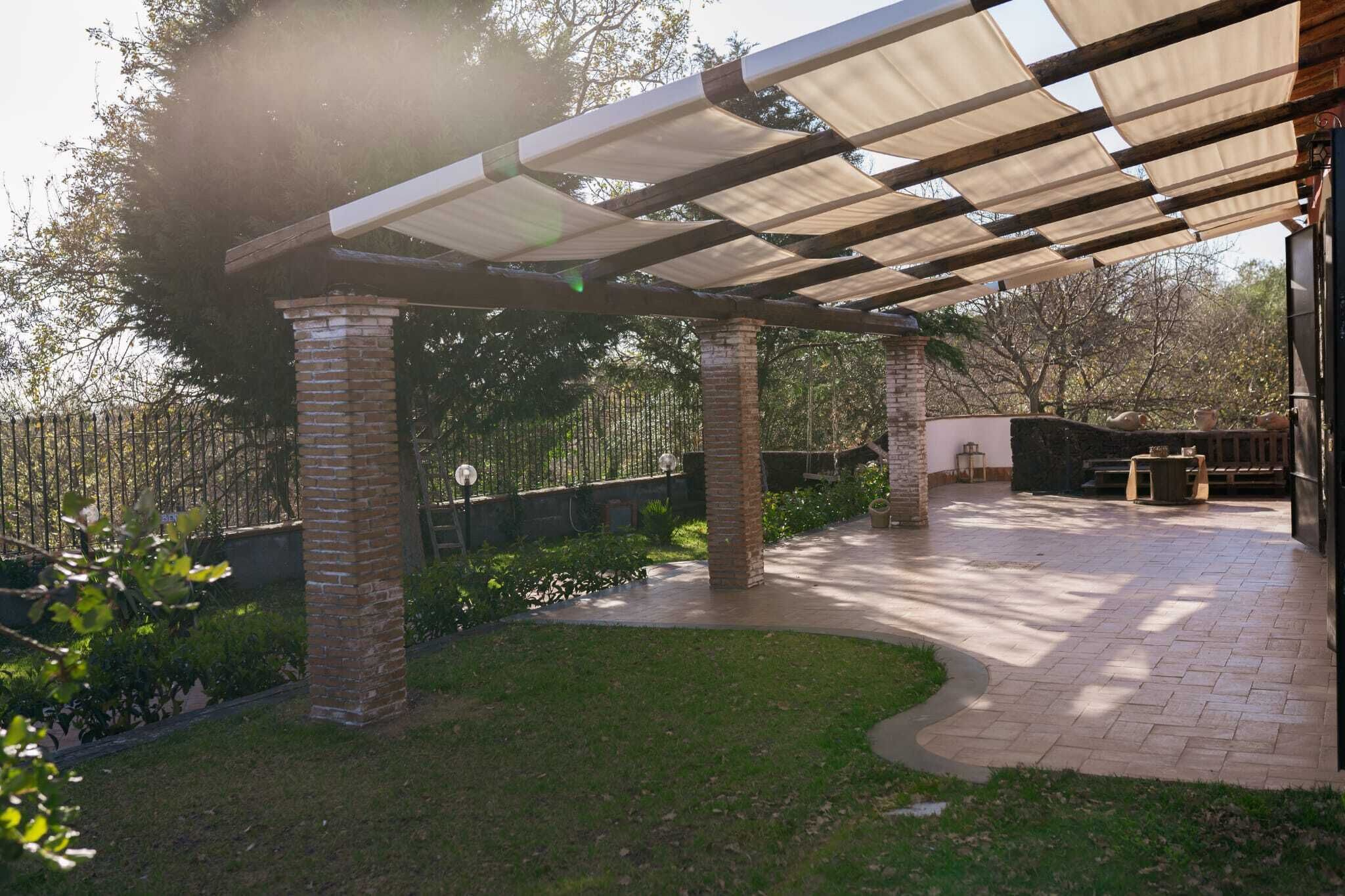 A covered patio area with brick pillars, a curved pathway, and a pergola providing shade.