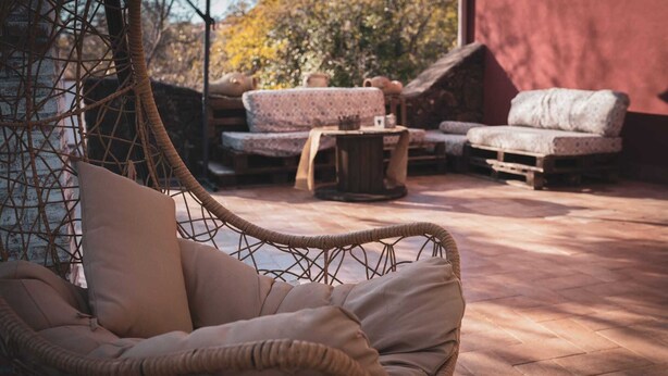 A wicker hanging chair with cushions, a patterned sofa, and a small table in an outdoor patio area with a tiled floor. - " il Rifugio di Aitna " (Ragalna)