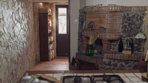 A rustic kitchen with a stone wall, a brick fireplace, and a wooden door leading to a hallway. - " il Rifugio di Aitna " (Ragalna)