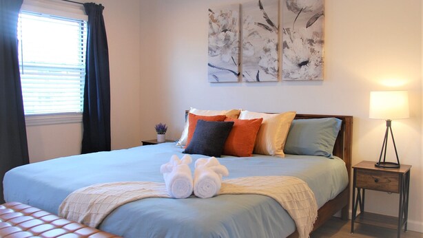 Una cama bien hecha con una colcha azul, varios almohadones y dos toallas enrolladas sobre la cama.